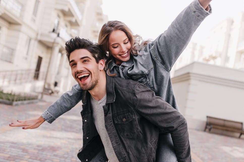 Pareja joven sonriendo mientras él la lleva en la espalda, representando vitalidad y bienestar general